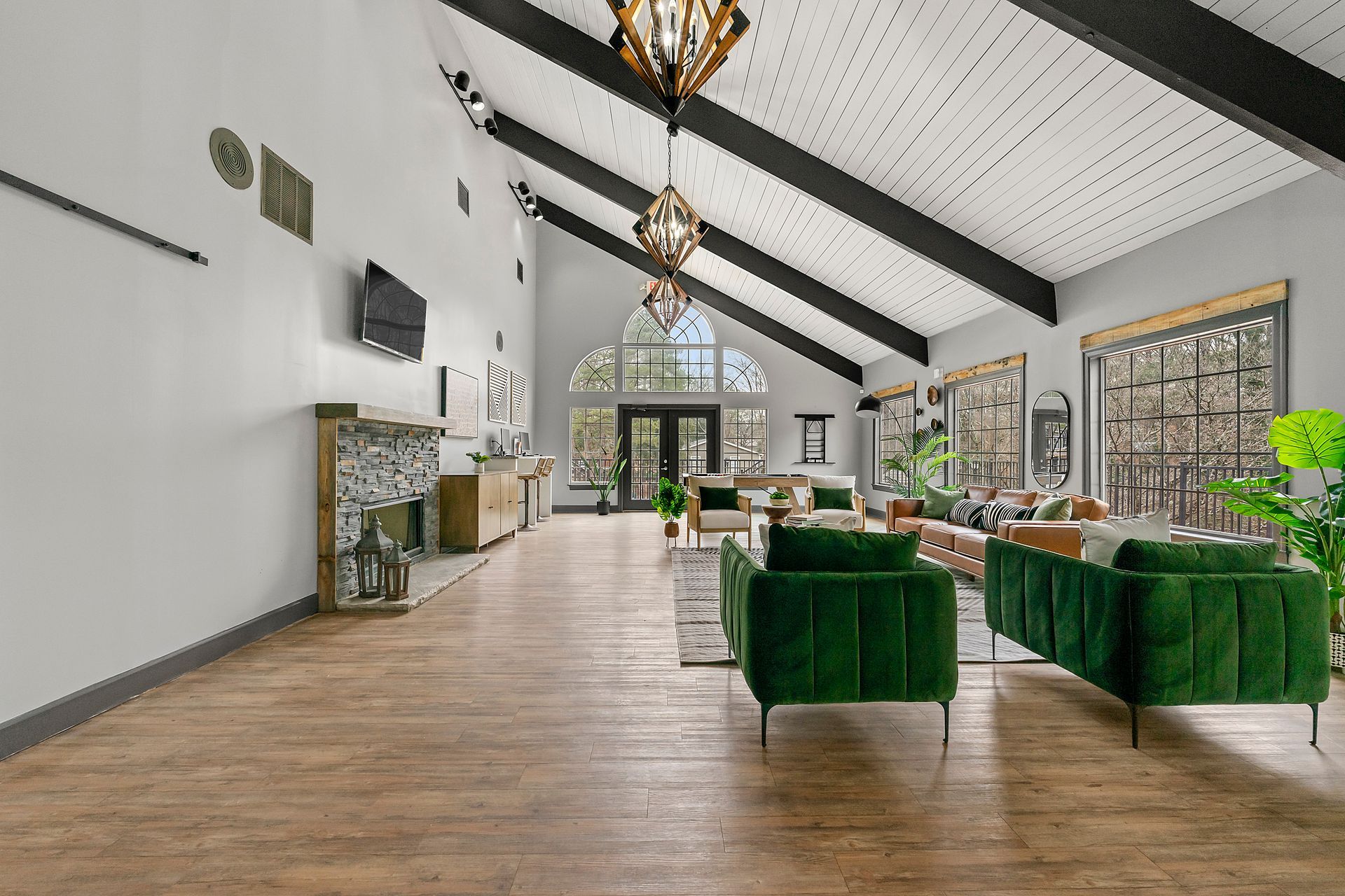 Bright modern living room with green sofas, wood floors, vaulted ceiling, and large windows