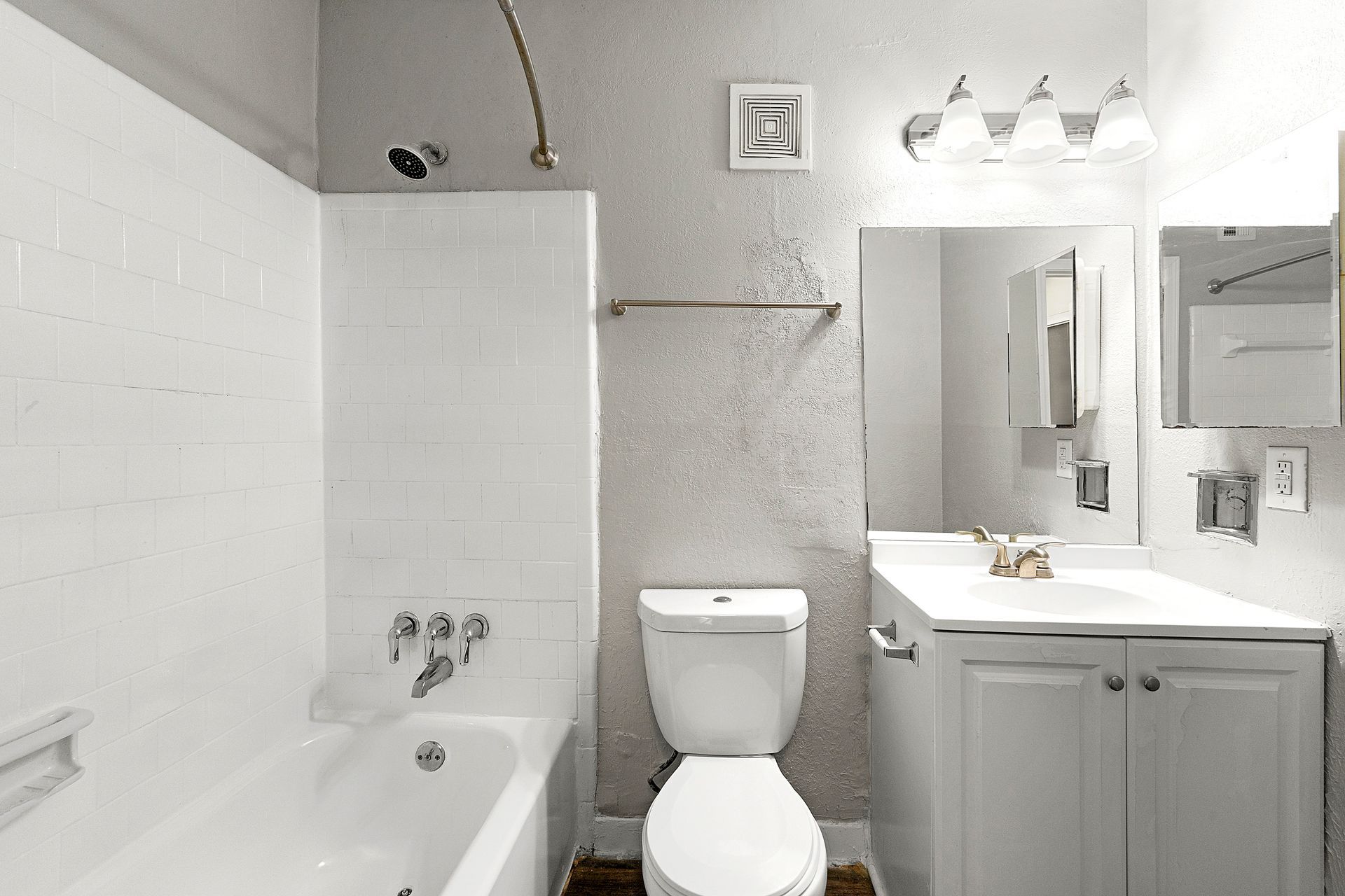 Bright bathroom with bathtub, toilet, vanity sink, mirror, and wall lights; white and gray decor.
