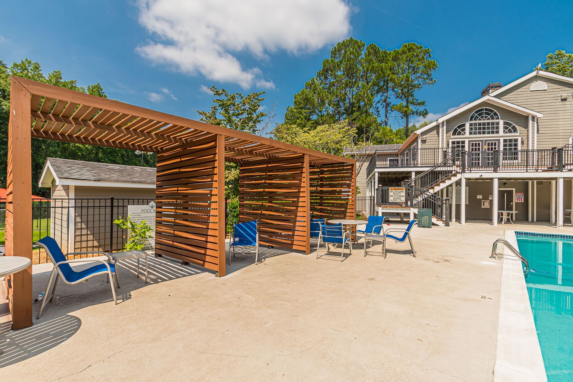 Luxury resort poolside with wooden cabanas, blue loungers, and a modern building under a sunny sky