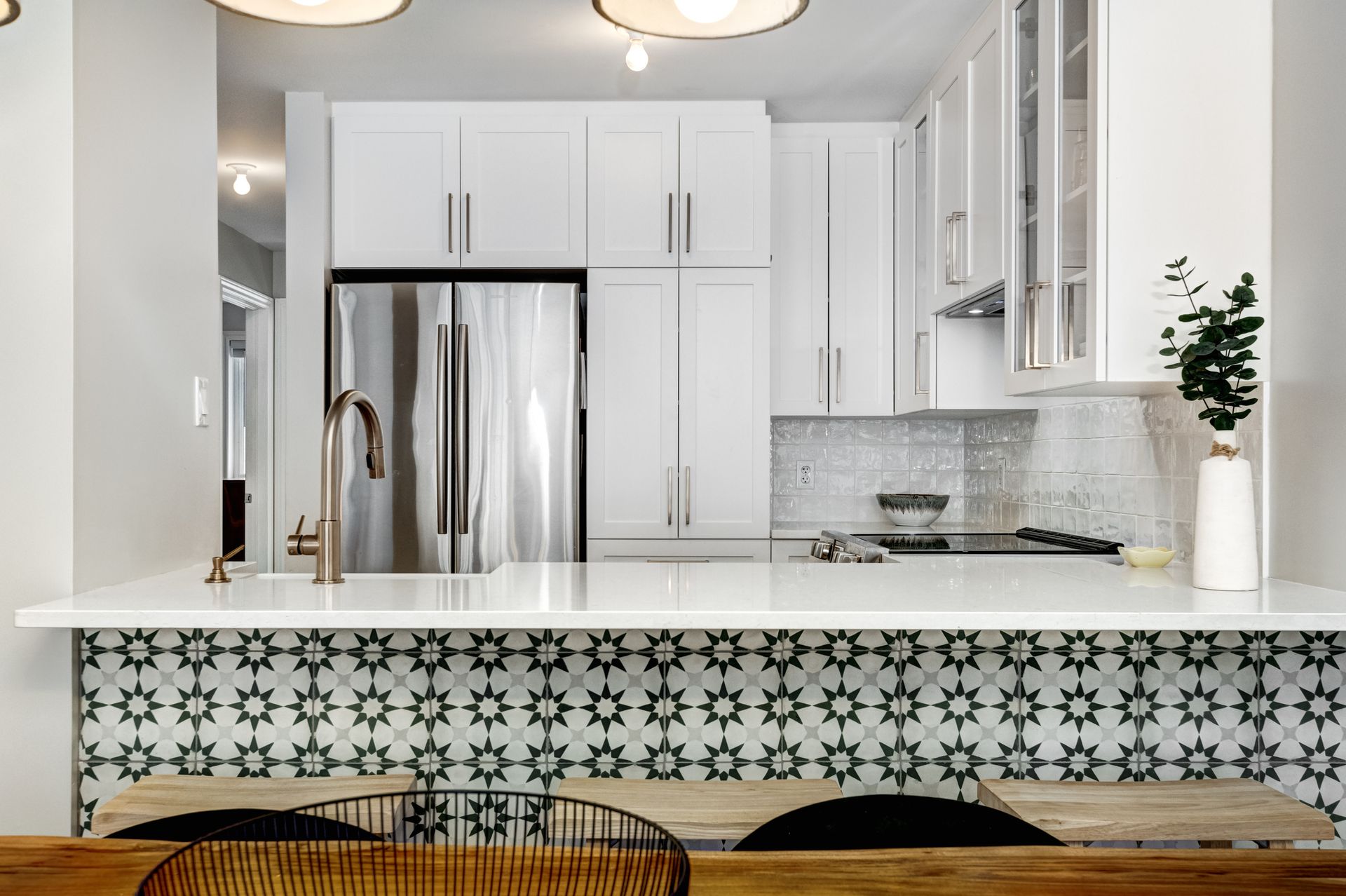 Bright kitchen with white cabinets, stainless fridge, patterned island front, and wooden bar stools