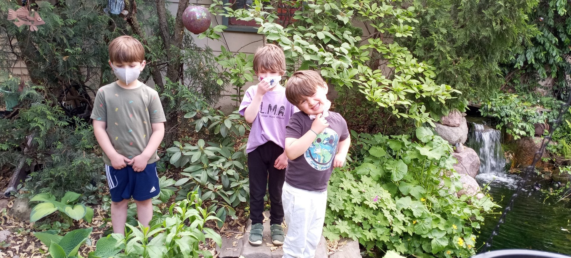 Three children are outdoors standing in between rows of greenery.