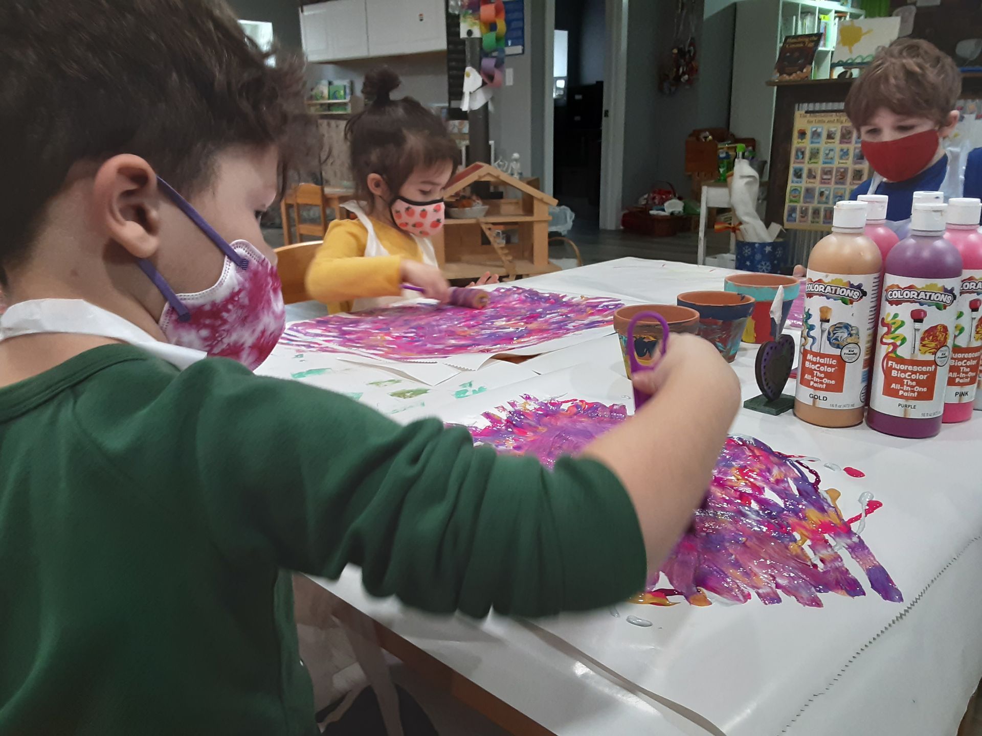 Three children are seated at a table fingerpainting.