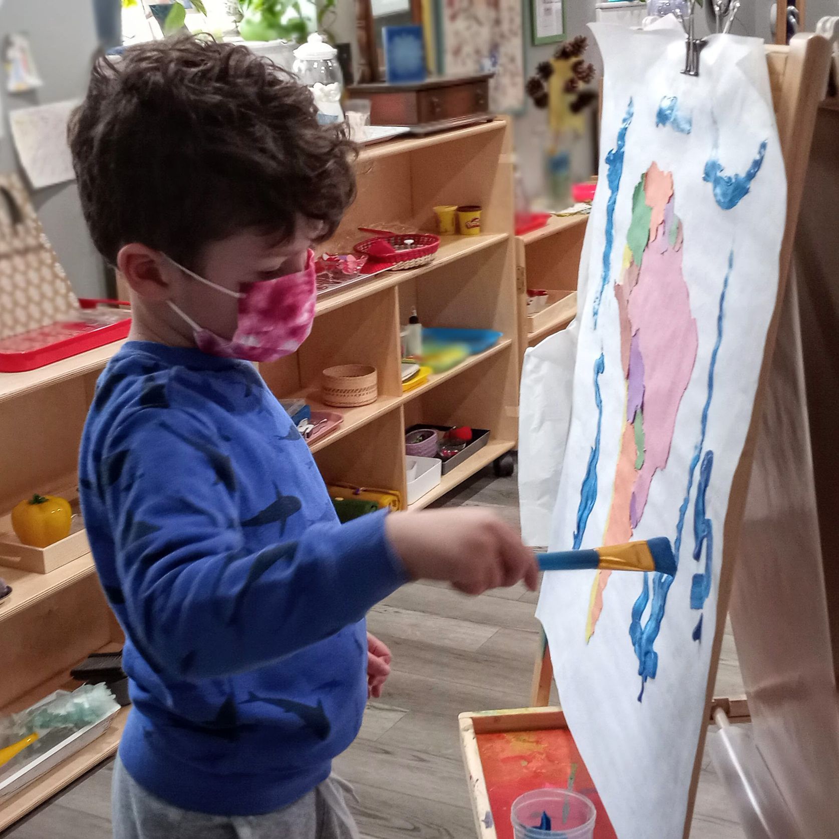 A child is painting a picture with a paintbrush at an easel.