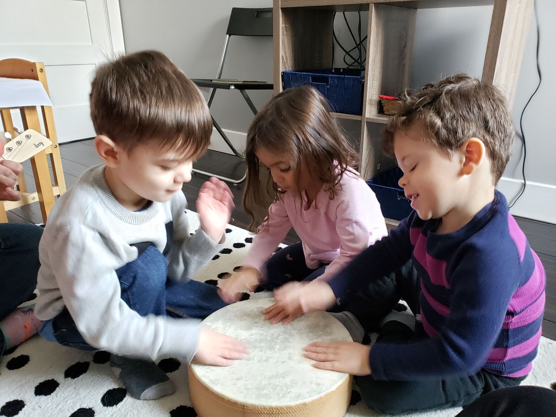 Three young children patting their hands on the surface of a drum.