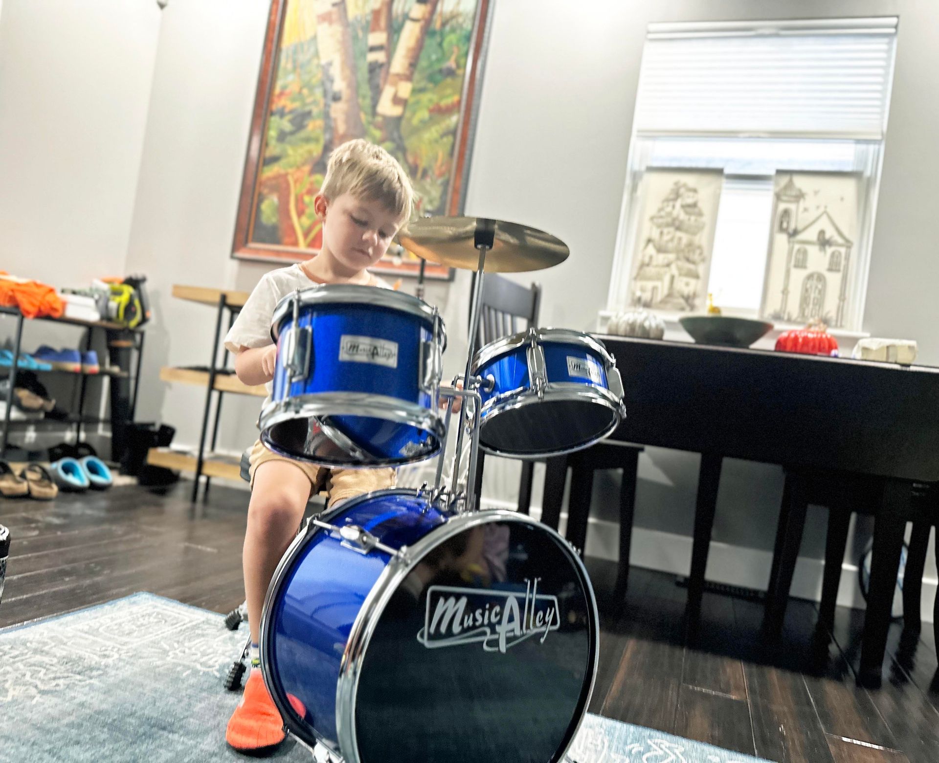 A child is seated with drumsticks behind a child-sized blue drum set, preparing to hit one of the drums.
