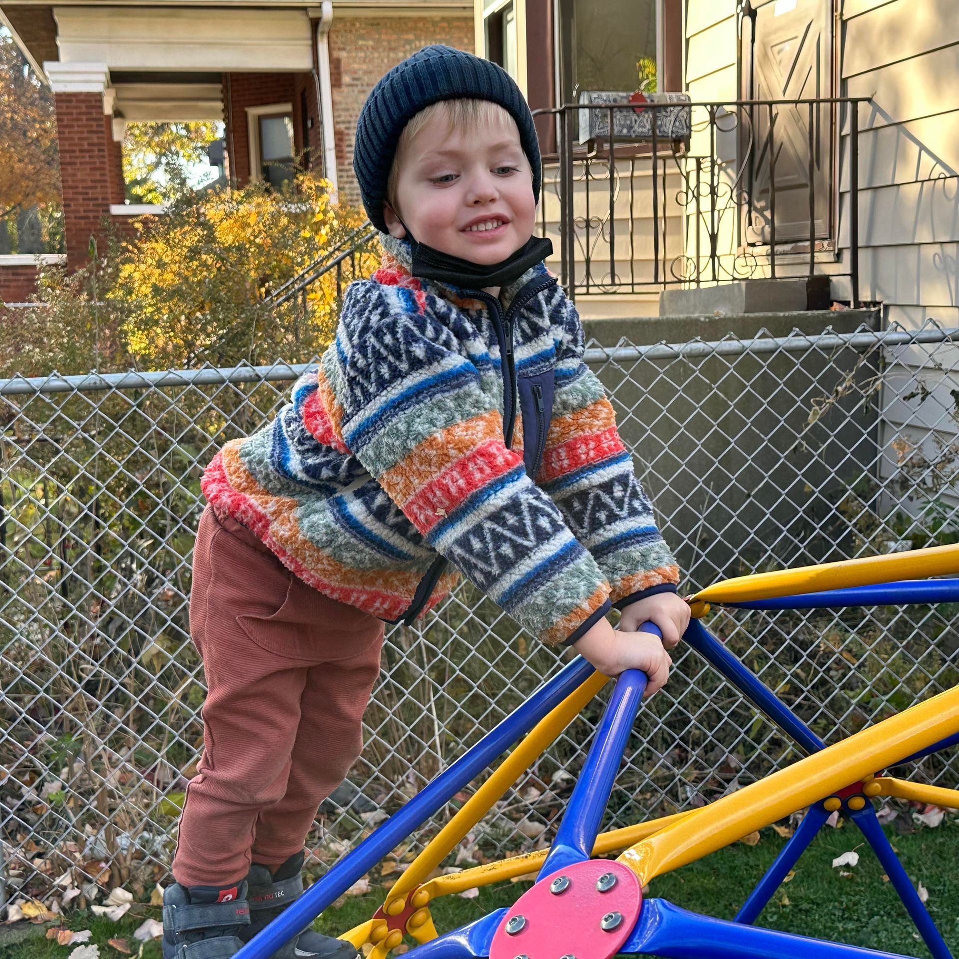 A smiling young child is posed near the top of a dome-shaped backyard climbing structure.