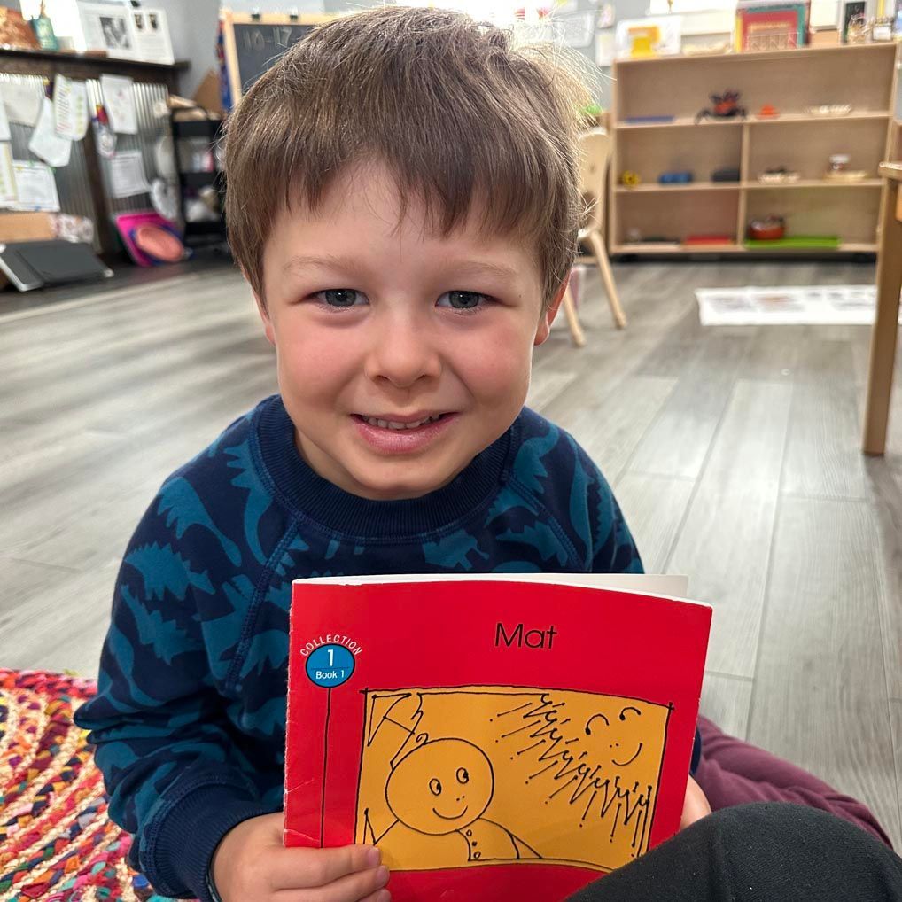 A young child seated on the floor holds a book.