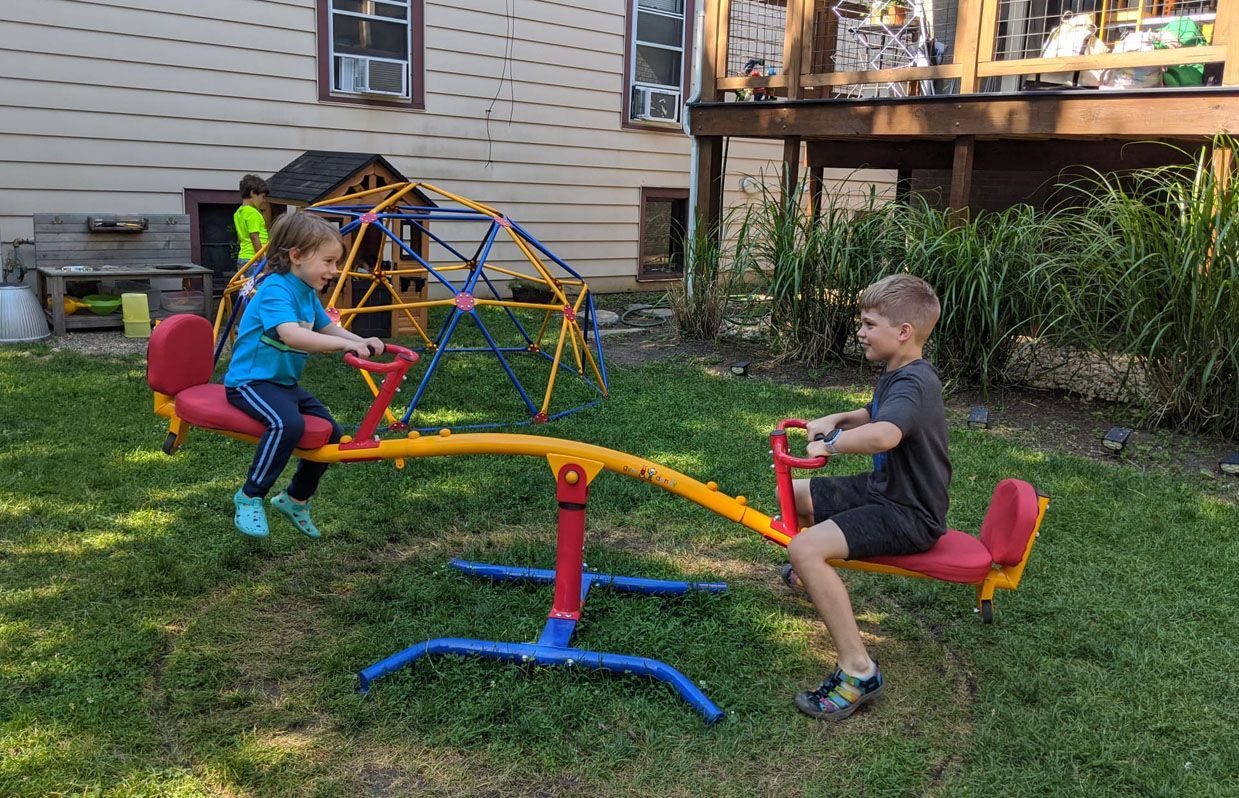 Two children outdoors on a backyard teeter-totter structure.