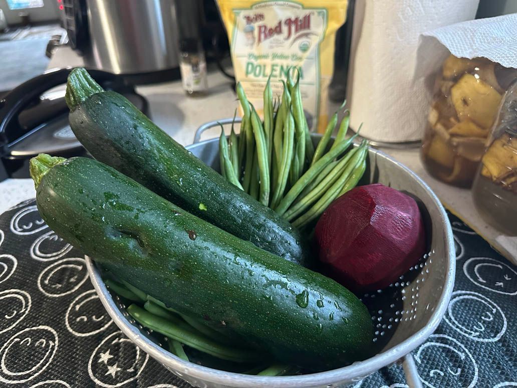 bowl of 2 whole zucchinis, several green beans and an onion