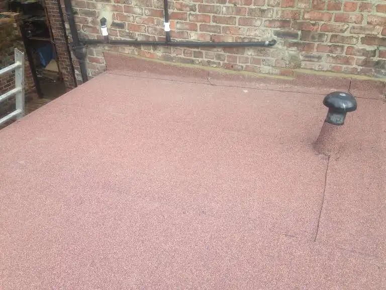 Red flat roof with a vent against a brick wall.