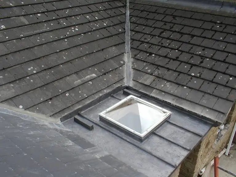 Slate roof with a skylight, showing overlapping tiles, lead flashing, and a gray sky.