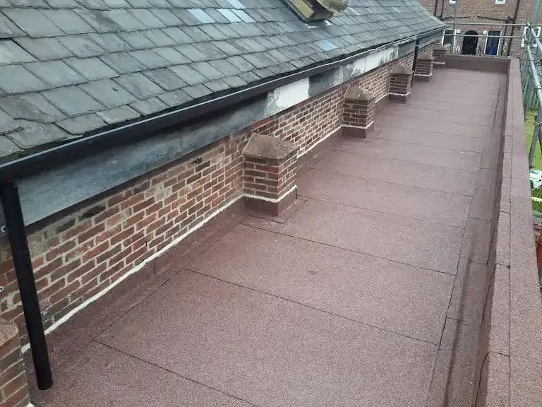 Flat, red-brown roof with brick wall and slate roof border; a gutter runs along the slate.