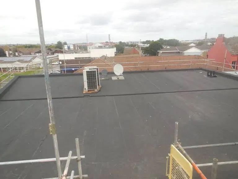 Black rooftop with equipment, scaffolding, and cityscape background under cloudy sky.