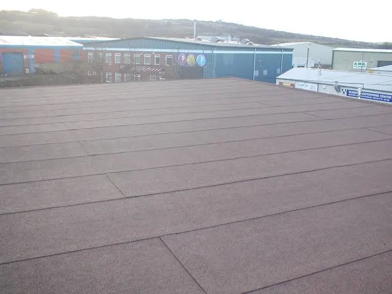 Flat, brown rooftop with dark lines, in front of industrial buildings.