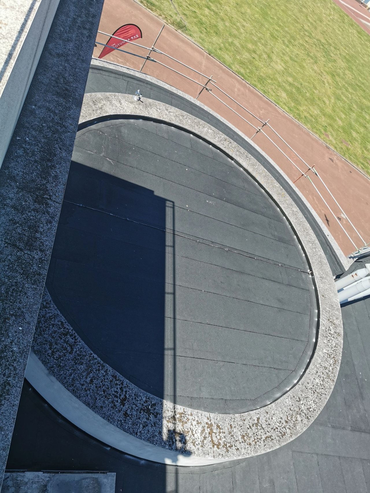 Overhead view of a circular black surface bordered by concrete. A red triangular flag is visible on adjacent track.