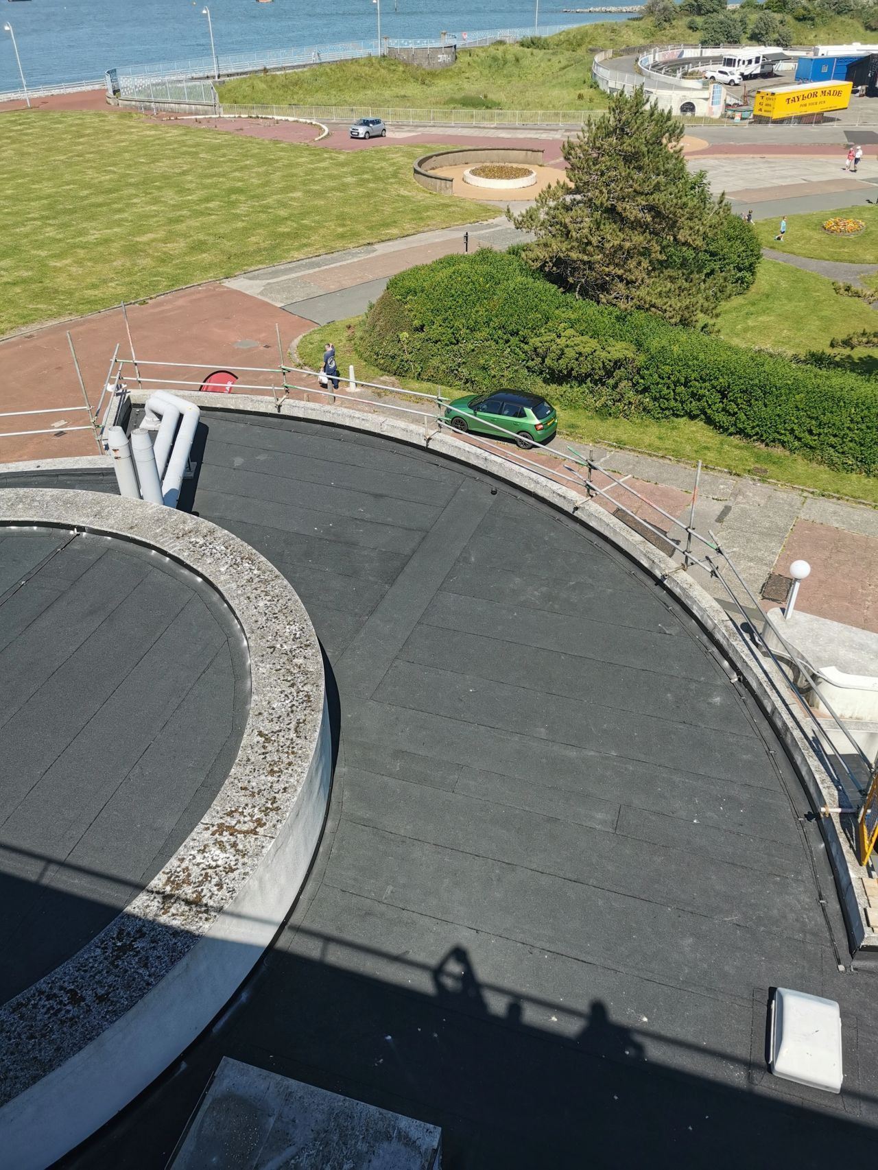 Overhead view of a curved road with a green car, near green grass and a bus stop.