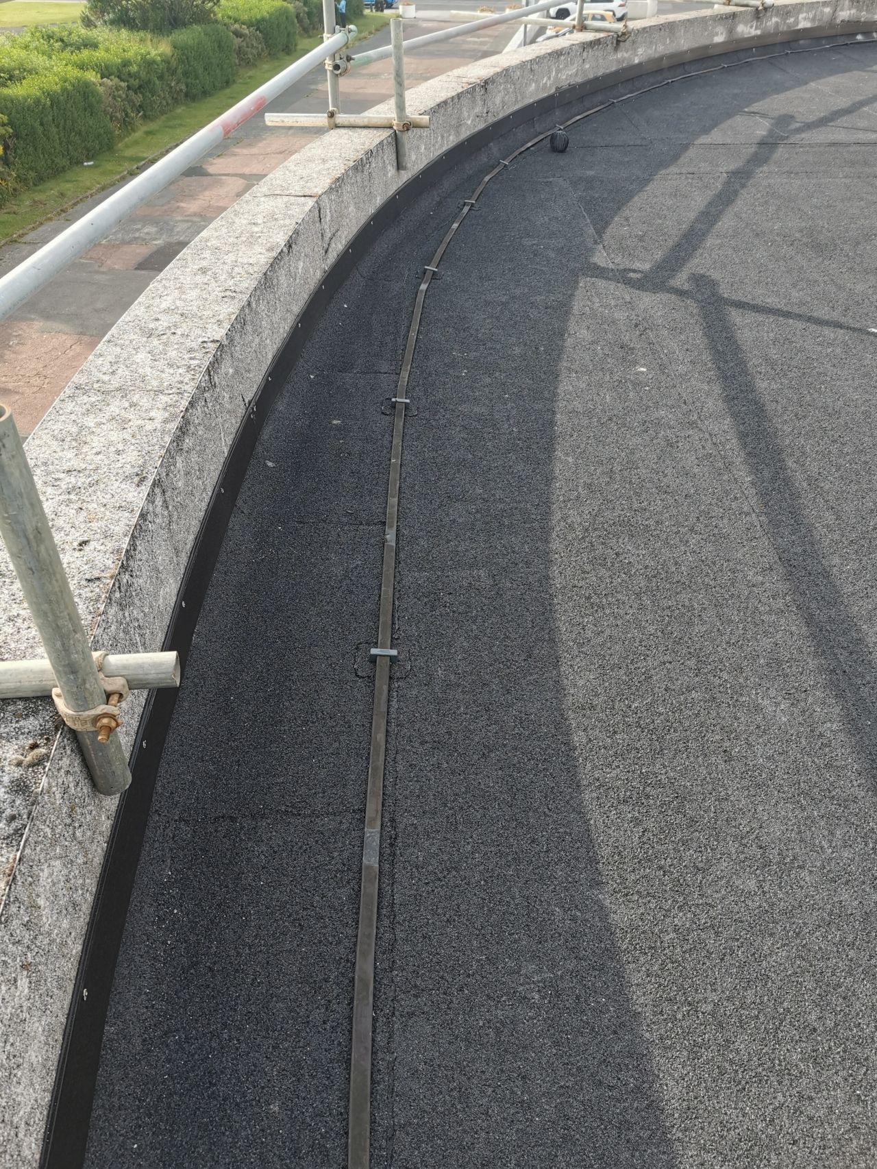 Curved concrete structure with dark, textured surface and a safety rail.