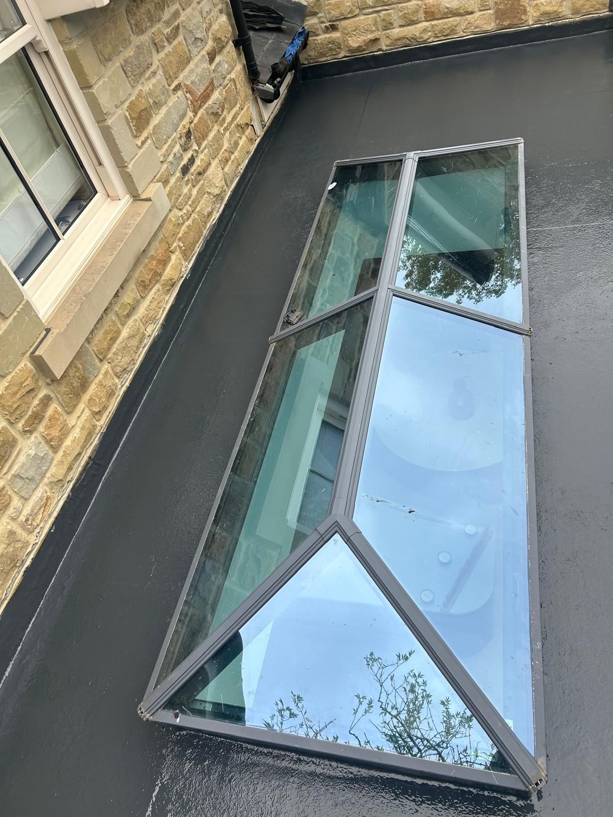 Rectangular skylight on a stone wall, reflecting the sky and nearby trees.