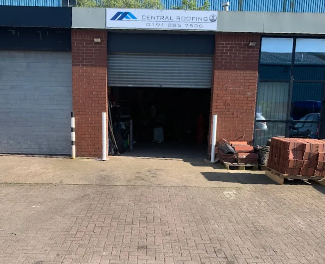 Brick building with Central Roofing sign, roll-up door open, exterior, daylight.