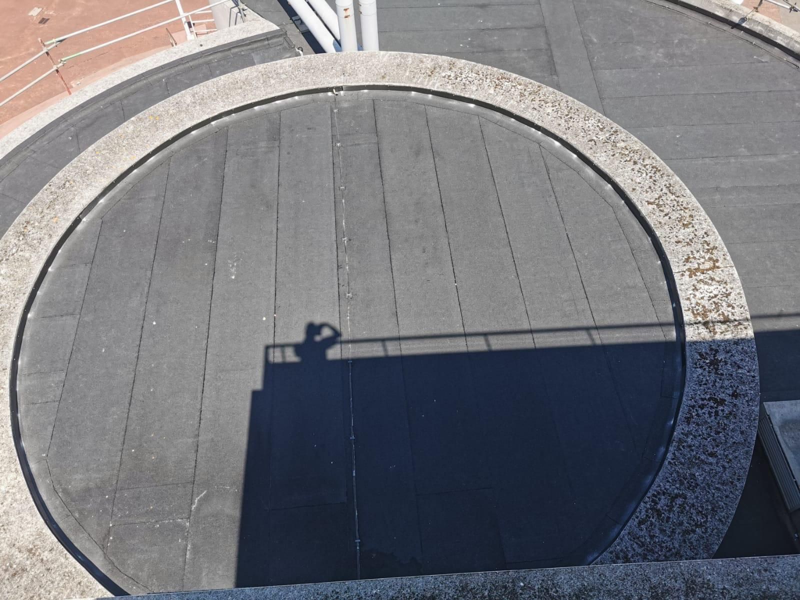 Overhead shot of a circular structure with a person's shadow, likely on a building's roof.
