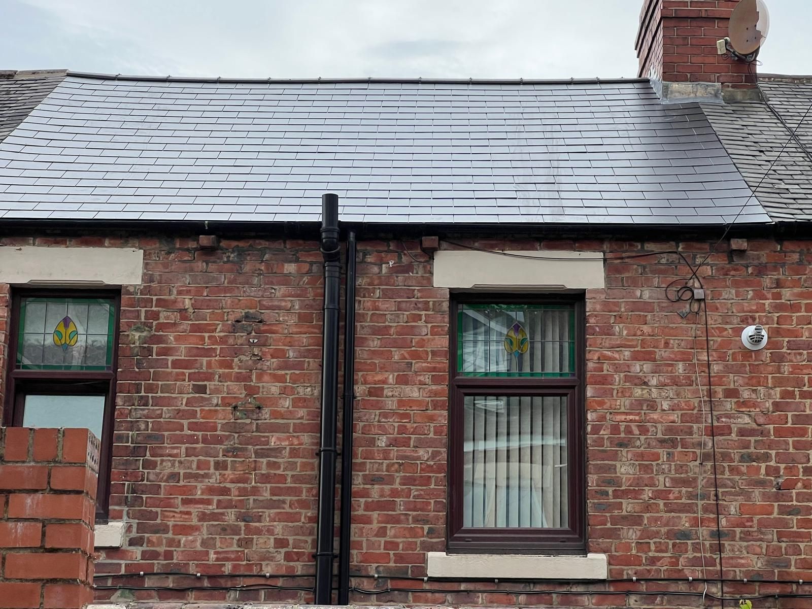 Brick house with dark roof and brown window frames; stained glass in the left window.