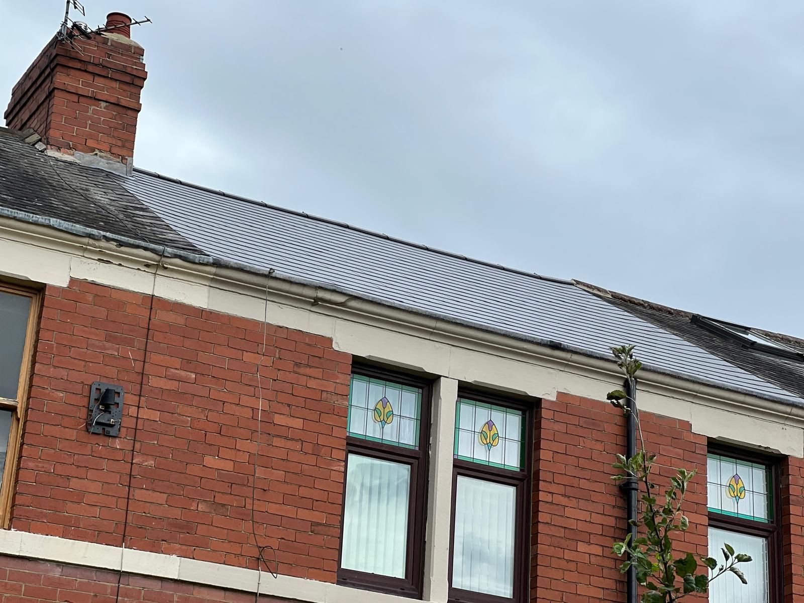 Red brick building with gray tiled roof and stained glass windows on a cloudy day.