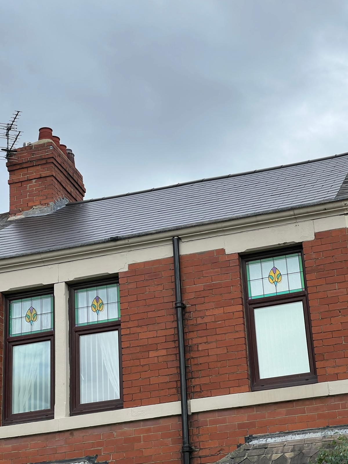 Red brick building with stained glass windows, slate roof, and a chimney against a cloudy sky.