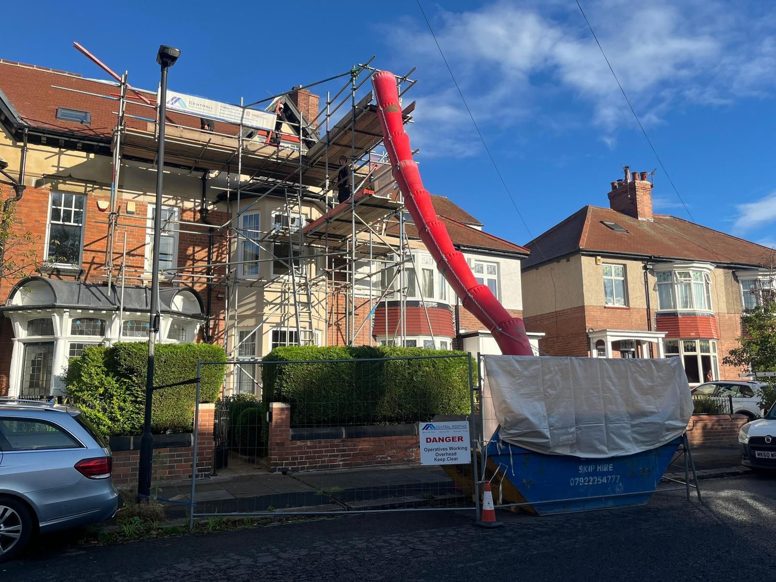 Scaffolding and red debris chute on a house, next to a skip.