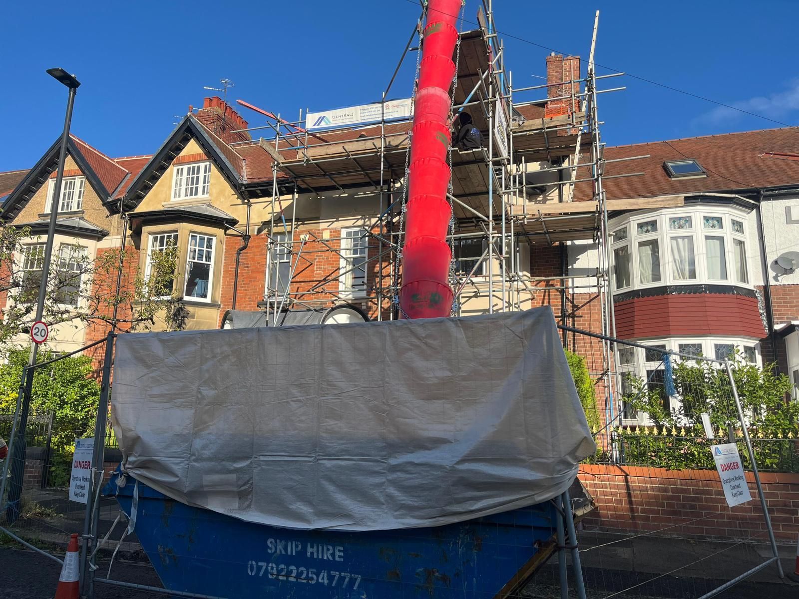 Residential building under renovation with scaffolding and a red debris chute.