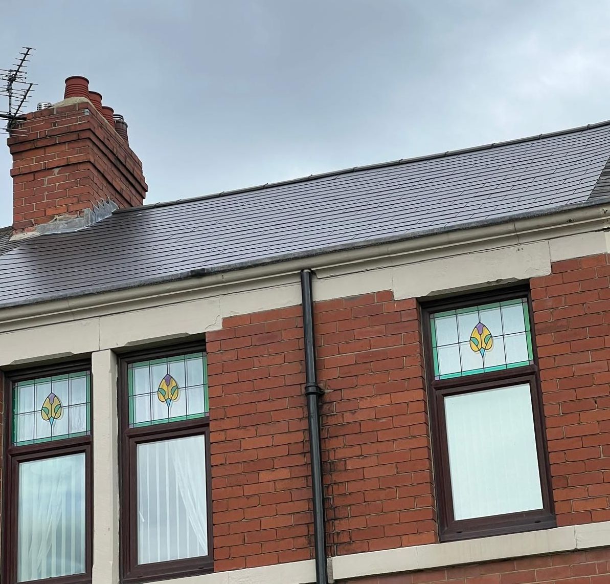 Brick building with stained glass windows and a slate roof against a cloudy sky.