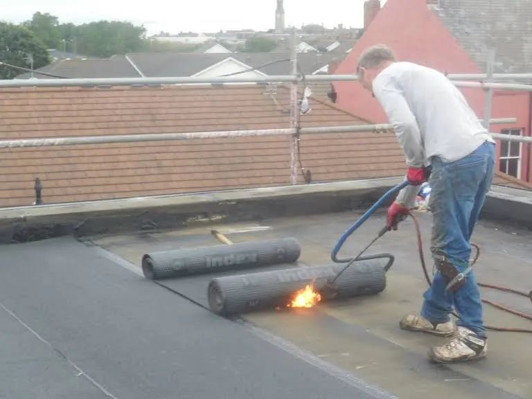 Roofer uses a torch to apply roofing material to a flat roof.