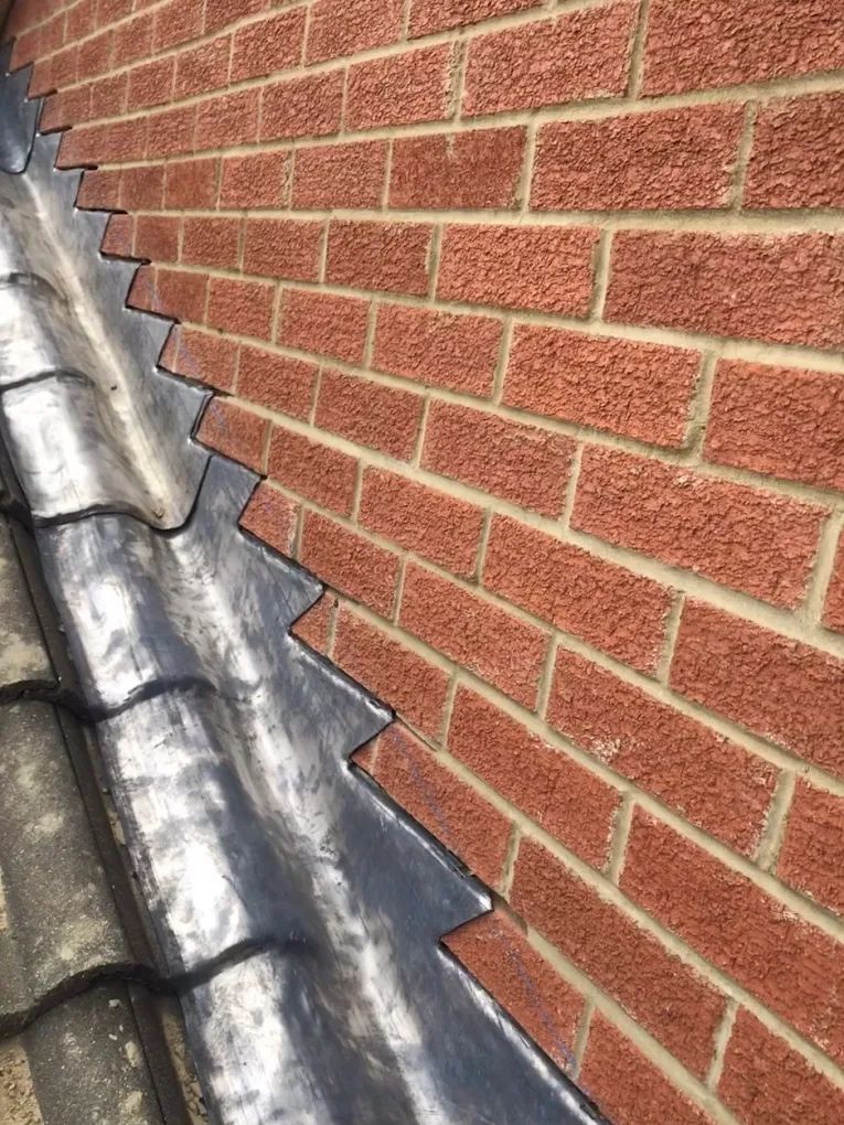 Close-up of a brick wall and roof tiles, showing lead flashing installed between them for waterproofing.
