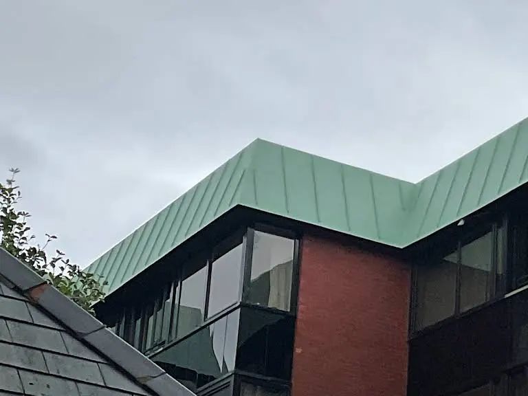Green metal roof on a brick building with large windows under a cloudy sky.