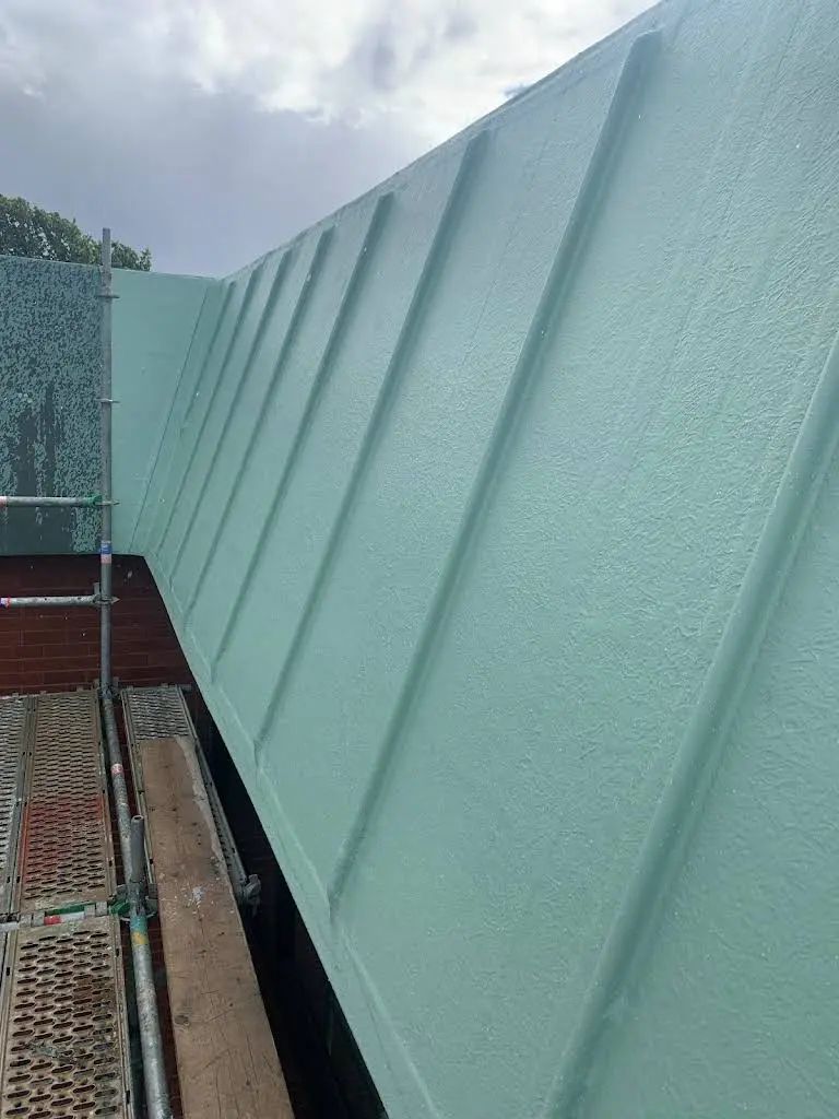 Green metal roof with diagonal lines. Scaffolding and brick visible below.