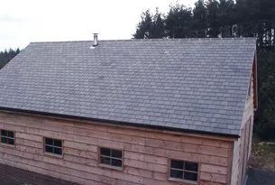 Wooden building with gray shingle roof, small windows, and a chimney. Trees in the background.