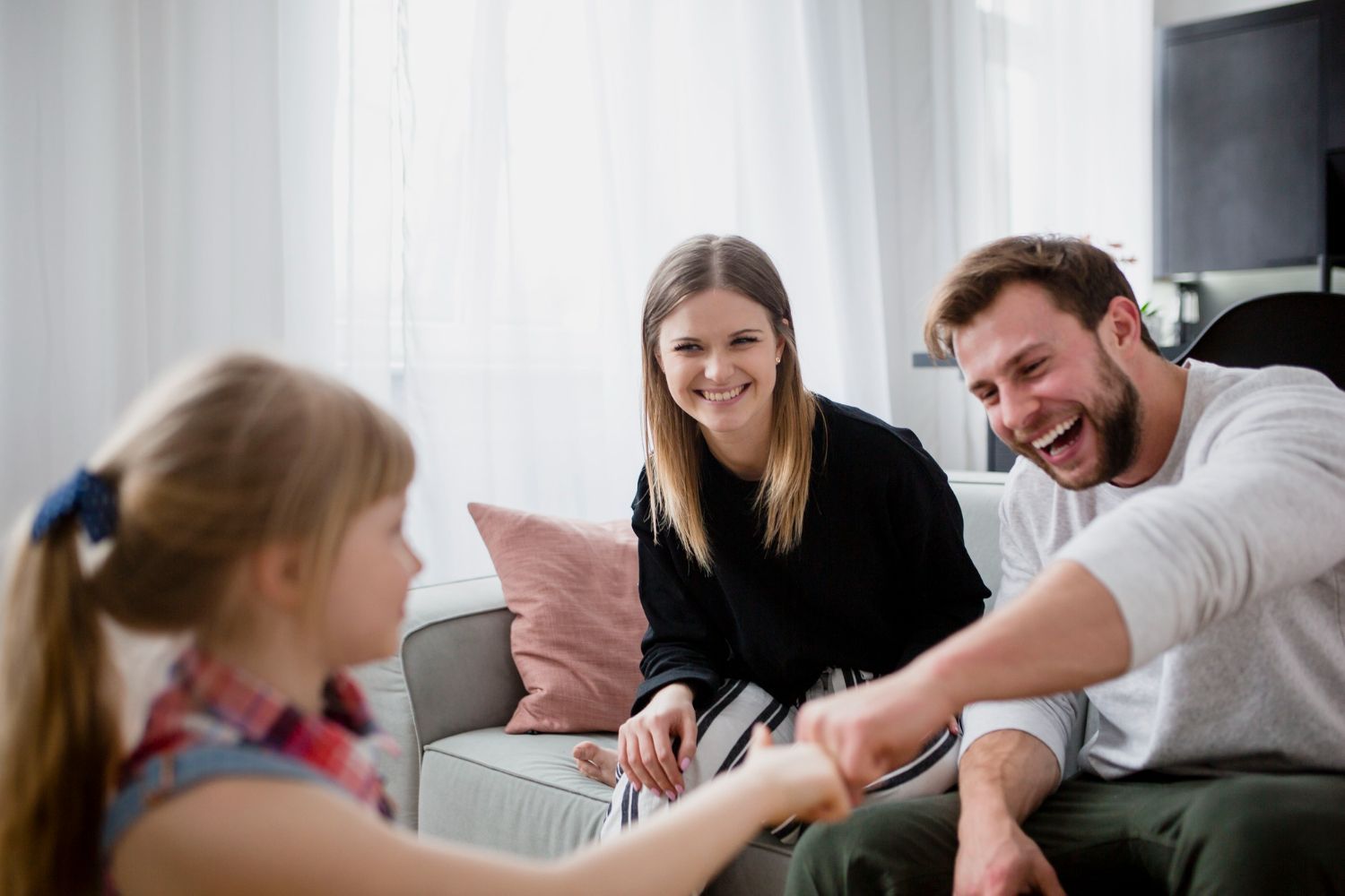 Three people smiling on a couch, reaching hands together in a bright living room