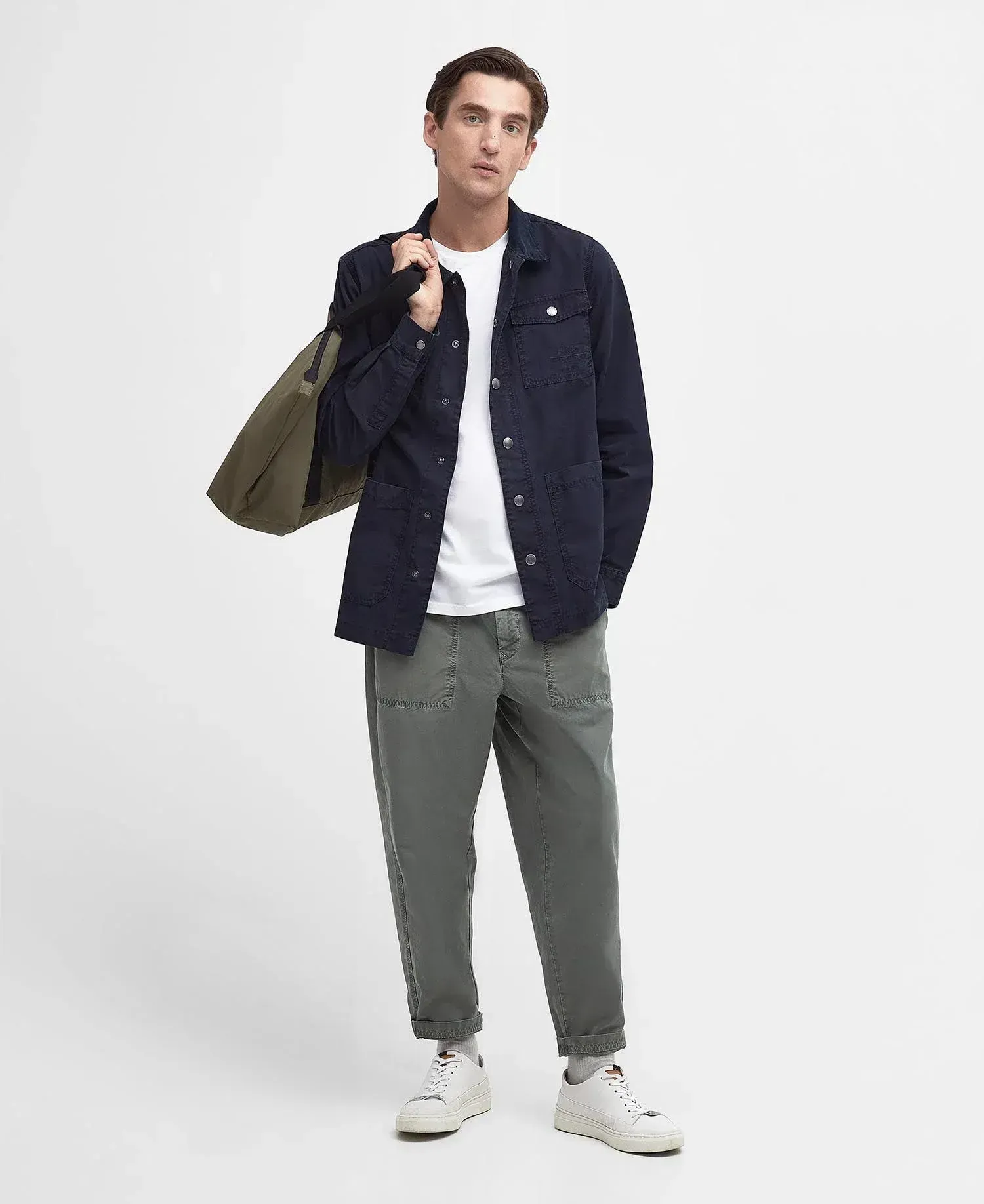 Un uomo che indossa una giacca blu e pantaloni verdi tiene in mano una borsa verde.
