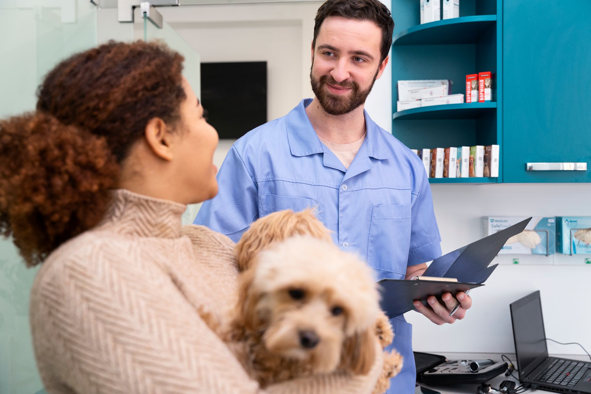 Mujer sosteniendo un perro en el veterinario y hablando con un veterinario con uniforme azul.