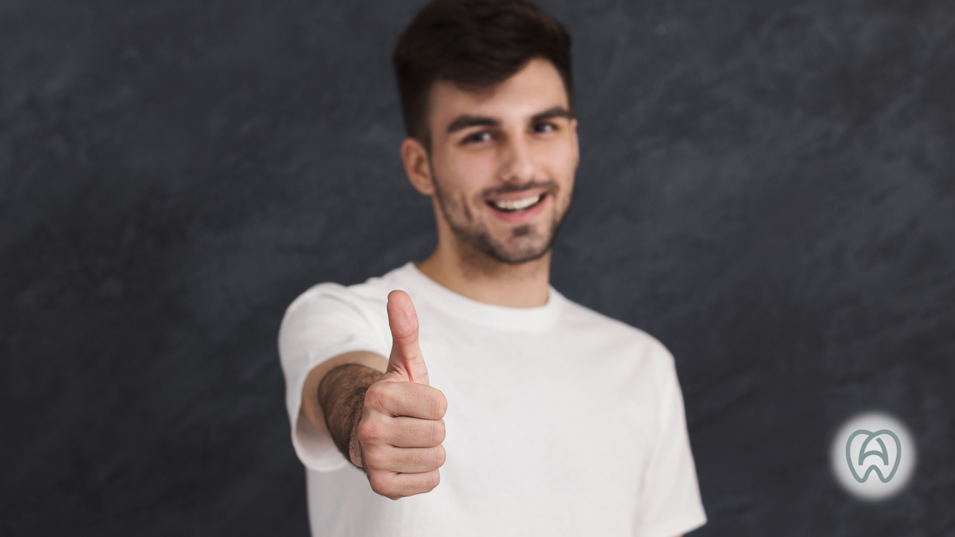 Smiling man in a white shirt giving a thumbs-up against a dark background