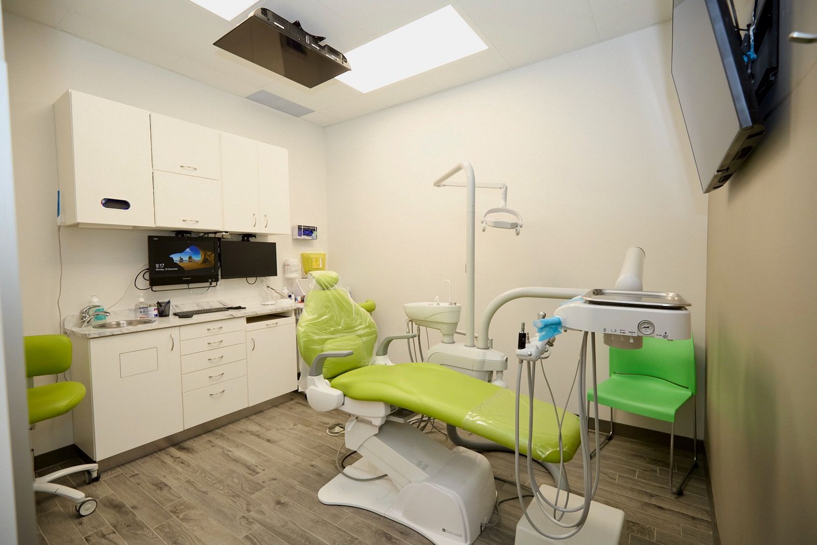 Dental exam room with a green chair, cabinets, and equipment.