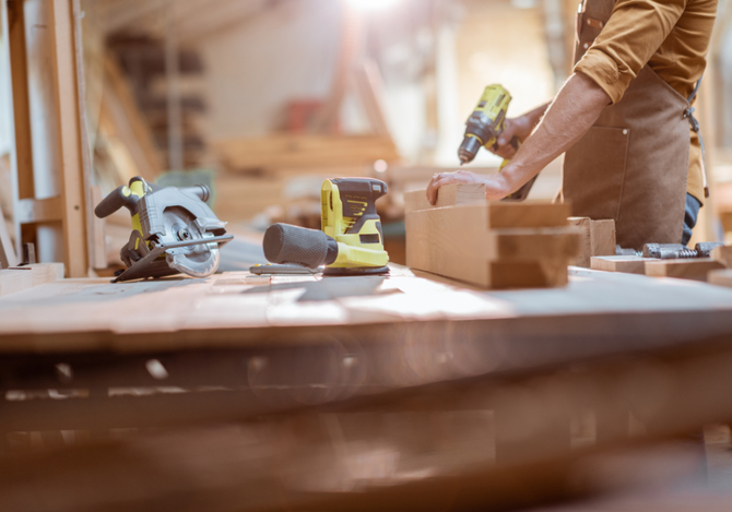 A man is working on a wooden table with a drill and a circular saw.
