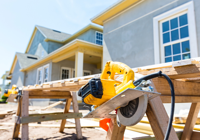 A circular saw is sitting on a wooden trestle in front of a house under construction.