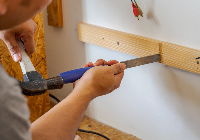 A person is using a hammer to hammer a piece of wood into a wall.