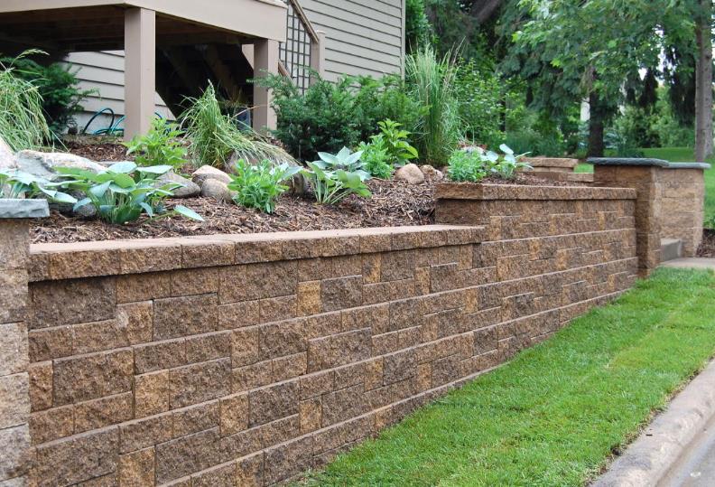 A brick wall with plants growing on it in front of a house.
