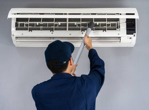 A man is cleaning an air conditioner with a vacuum cleaner.