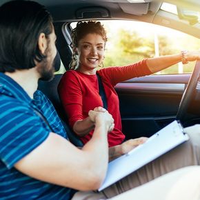 a woman and a man shaking hands in a car after a driving lesson