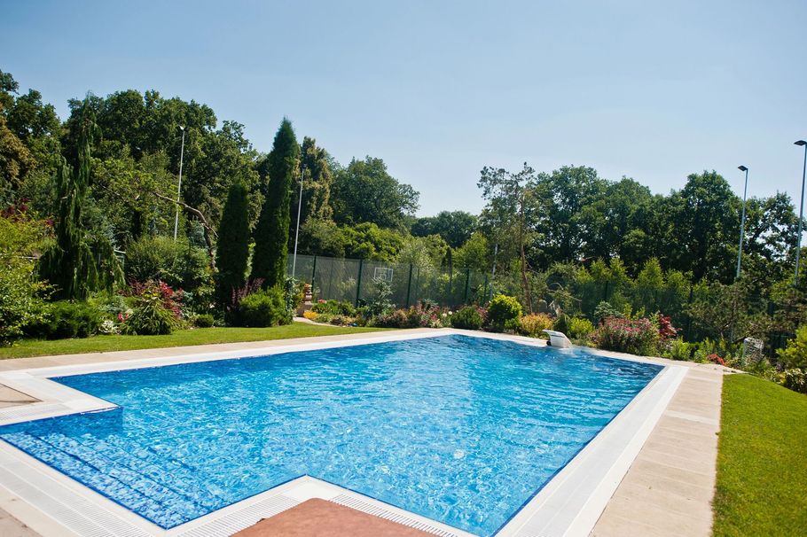 Piscina all'aperto con acqua di un azzurro brillante, circondata da una terrazza pavimentata e da rigogliosi alberi verdi.