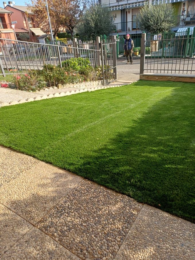 Prato verde appena falciato accanto a un sentiero lastricato e a una recinzione metallica in un giardino residenziale.