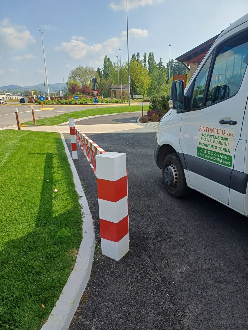 Barriera di parcheggio rossa e bianca accanto a un furgone di servizio bianco su una strada asfaltata vicino a un'area erbosa.