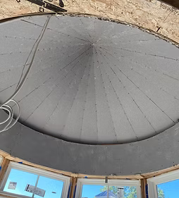 Large gray circular ceiling dome with window openings around the base in a timber-framed room